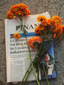Marigold flowers on financial newspaper symbolize economic reflection. Warm afternoon light.